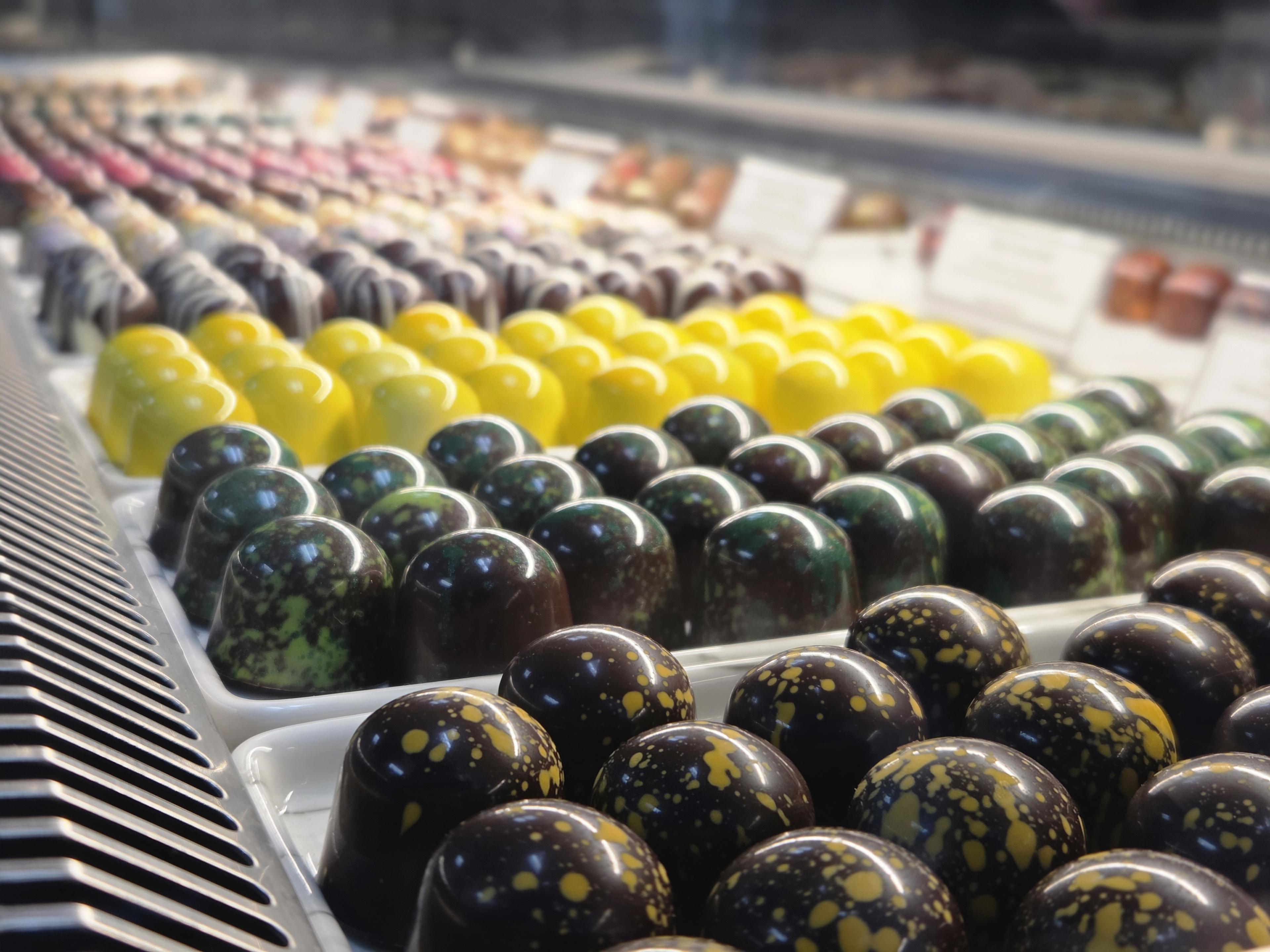 A single bonbon with a gold and dark chocolate airbrushed shell, on white marble